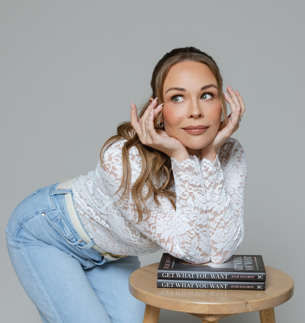 Julie Solomon leaning on a stool beside copies of her book Get What You Want