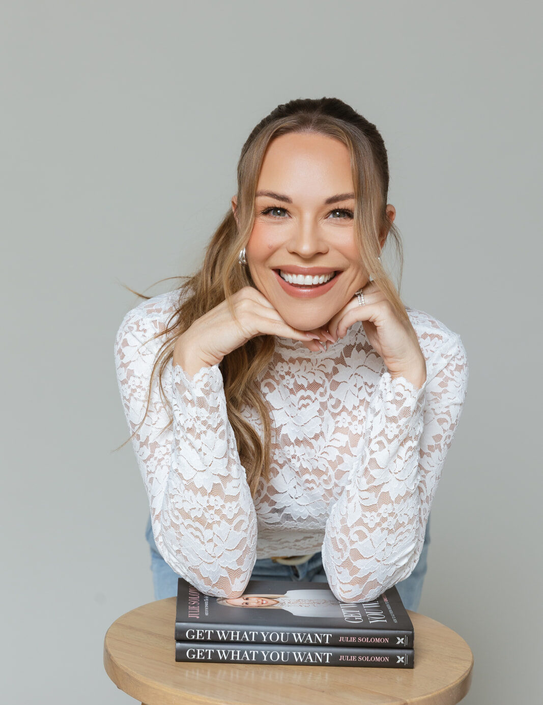 Julie Solomon in a white lace top with her chin on her hands beside her book